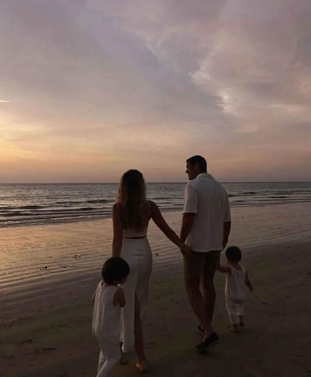 Families: a couple and their two children walking on the beach at sunset